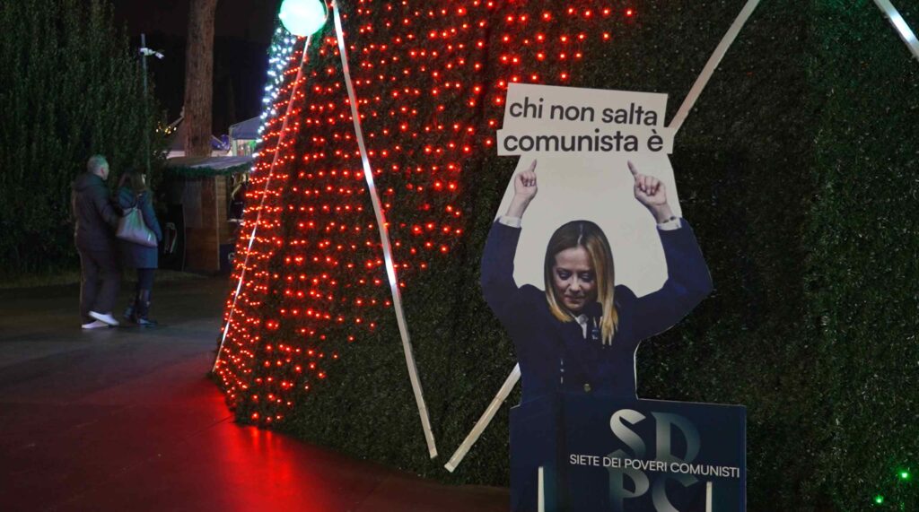 Carton montrant Meloni tenant un panneau "chi non salta comunista è"