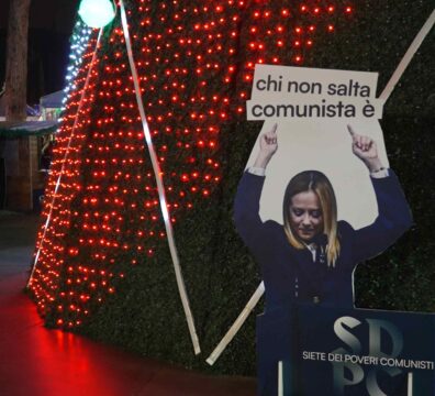 Carton montrant Meloni tenant un panneau "chi non salta comunista è"