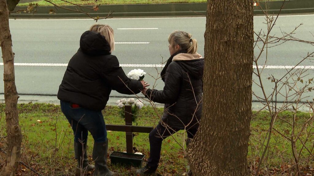 Une mère et sa fille déposent des fleurs auprès d'une croix.