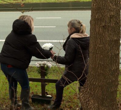 Une mère et sa fille déposent des fleurs auprès d'une croix.